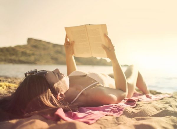 Mulher na praia com livros para ler nas fériasol